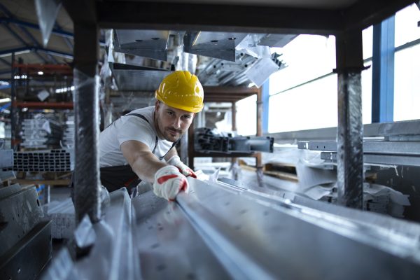 Factory worker working in warehouse handling metal material for production.